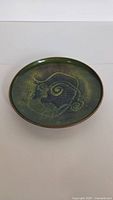 Top angled view of round copper enameled dish with decorative abstract pattern in green and black.