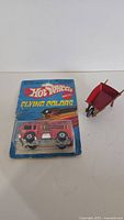 Red Hot Wheels Fire Eater fire truck toy in original blister card packaging and a red metal wheelbarrow toy.