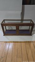 Full front view of oak glass display case showing rectangular shape, double doors, and top glass panel.