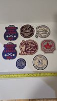 Top view of the full set of 8 vintage Dundas sports patches on a white background with tape measure for scale, showing condition and designs.