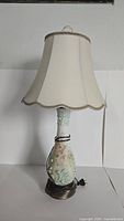 Full view of vintage hand painted table lamp with cream scalloped fabric shade and floral painted ceramic base on bronze stand.