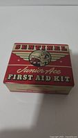 Top view of the unopened metal box featuring vintage Sentinel Junior Ace First Aid Kit graphics.