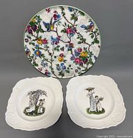 Front view of two white square Kate Greenaway plates illustrating Victorian children, and one colorful round Royal Tudor Ware cake plate featuring floral and bird motifs.