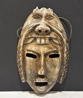 Front view of double face carved stone tribal mask showing primary human face with eyes and mouth cut out and secondary animal-like face on forehead.