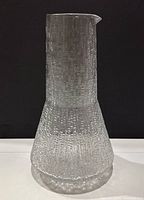 Front view of textured clear glass carafe with bark-like pattern and pouring spout.