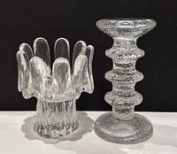 Two clear textured glass candlesticks side by side on white surface, black background, showing overall shapes and texture.