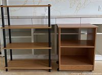 Front view of two shelving units: a four-tier wood and black metal shelving unit and a microwave stand with two shelves, both on caster wheels.