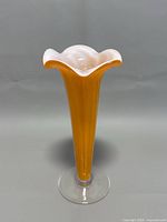 Front right angled view of the orange and white glass vase showing the ruffled top and clear base.