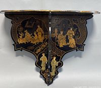 Front view of black lacquer wall shelf with detailed hand painted Asian figures in gold and muted colors, floral designs around edges.