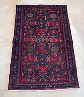 Photo showing full view of the rectangular vintage Persian rug laid flat, highlighting the detailed floral and geometric design against a dark navy background with red and green accents.