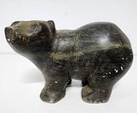 Side angle view of the dark stone bear sculpture showing its shape and condition including surface marks and scratches.