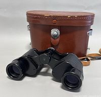 Pair of black vintage binoculars in front of original brown leather case with silver clasp and leather strap.