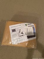 Photo of packaged beige nylon shade sail with installation instructions visible through plastic.