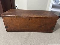 Closed view of rectangular wooden antique trunk showing wood grain and metal hardware on corners and front