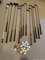 Full view of 14 golf clubs, including drivers, irons, wedges, and putter, plus a collection of golf balls and tees laid out.