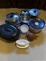 All items displayed together on carpeted floor, showing full contents of set including pots, teapot, roasting pan, gravy boat, and Crock-Pot.