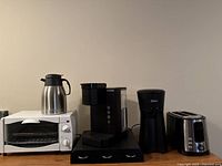 Wide shot of all small kitchen appliances lined up on counter: toaster oven, coffee carafe, Keurig machine, drip coffee maker, toaster