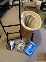 Wicker laundry basket with removable beige fabric liner, Black & Decker iron, dryer vent lint brush, Steam Express ball in package, and toilet auger on carpeted floor.
