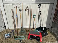 Full set of garden tools and garden sitting trolley arranged against white fence outdoors.