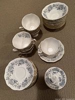 Photo showing stack of 7 teacups, 10 saucers, 11 pickle plates, and 11 dessert bowls with Silver Birch pattern in grey on white bone china with gold rim.