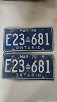 Photo showing front sides of the two matching 1978 Ontario license plates with blue background, white embossed text 'E23 681' and crown symbol. Plates show some wear and scratches.