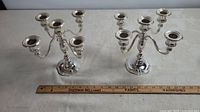 Pair of silver finish 5-arm candelabras placed side-by-side with a ruler for scale showing approximately 8.5 inches height.