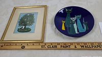 Framed art and enameled cat dish side by side with ruler for scale