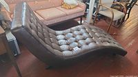 Side angle showing entire tufted chaise lounge with curved profile and metal legs.