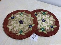 Photo showing pair of hooked chair seat covers with floral design and reddish borders.