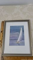 Photo showing the framed artwork including ruler for size reference, artwork depicts a sailboat with 'Y120' sail on calm water.