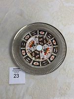 Top view of round porcelain plate with Imari 2451 pattern and silver lattice rim on cream tablecloth, showing color and design details