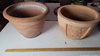 Two terracotta pots side by side on a table with a ruler for scale, measuring approximately 10-12 inches tall
