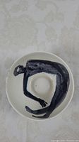 Top view of white ceramic bowl with black abstract human figure curled inside.