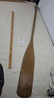 Full view of wooden paddle next to a measuring stick showing approximate length of 60 inches