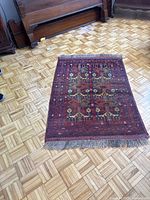 Full view of Afghan Baluch rug on parquet floor showing geometric pattern and fringed edges