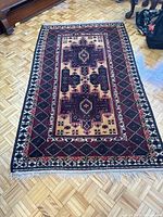 Full view of the Afghan tribal rug placed on parquet flooring showing the geometric and medallion center design, highlighting rich red, black, and beige patterns.