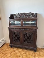 Front view of entire two-piece teak cabinet with carved doors and glass display top