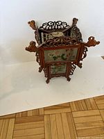 Three-quarter front view of square carved wood lantern showing two floral glass panels and scrollwork frame