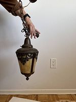 Hanging light held up showing the opaque glass panels, detailed metal ornamentation, chain, and mounting plate