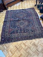 Top view of the entire flat rug showing geometric central motifs and multiple border patterns with fringe edges, laid on parquet flooring.