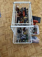 Top down view of wire basket containing various tools including an electric planer, tape measures, flashlight, and small hardware boxes.