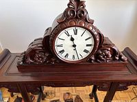 Front view of carved dark wood mantle clock showing ornate floral and scroll carving, round face with Roman numerals