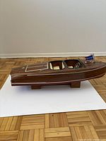 Side profile of the wooden hull on a white board showing varnished planking, pinstripes and display stand