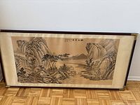 Full view of framed Chinese landscape artwork on floor showing mountainous scene, water and buildings