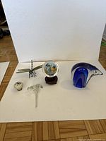 Lot of five glass ornaments arranged on white background showing blue polar bear, dragonfly sculpture, tiger glass globe, glass flower, and glass doorknob.