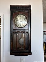 Front view of the Gustav Becker wall clock showing the wooden case, clock face, and glass door.