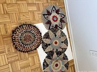 Four round hand-sewn vintage seat cushions arranged on a light wood parquet floor showing multicolored patterns on the top side.