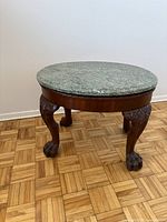 Front angled view of round table showing green marble top and carved claw feet wooden legs