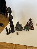 Photo of seven oriental figurines placed on a white background. Includes wooden tribal carvings, metal figure, and elephant figurines.