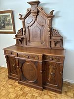 Front angle view of the walnut Renaissance Revival sideboard showing ornate carved backboard, drawers, and cabinet doors with burl wood panels.
